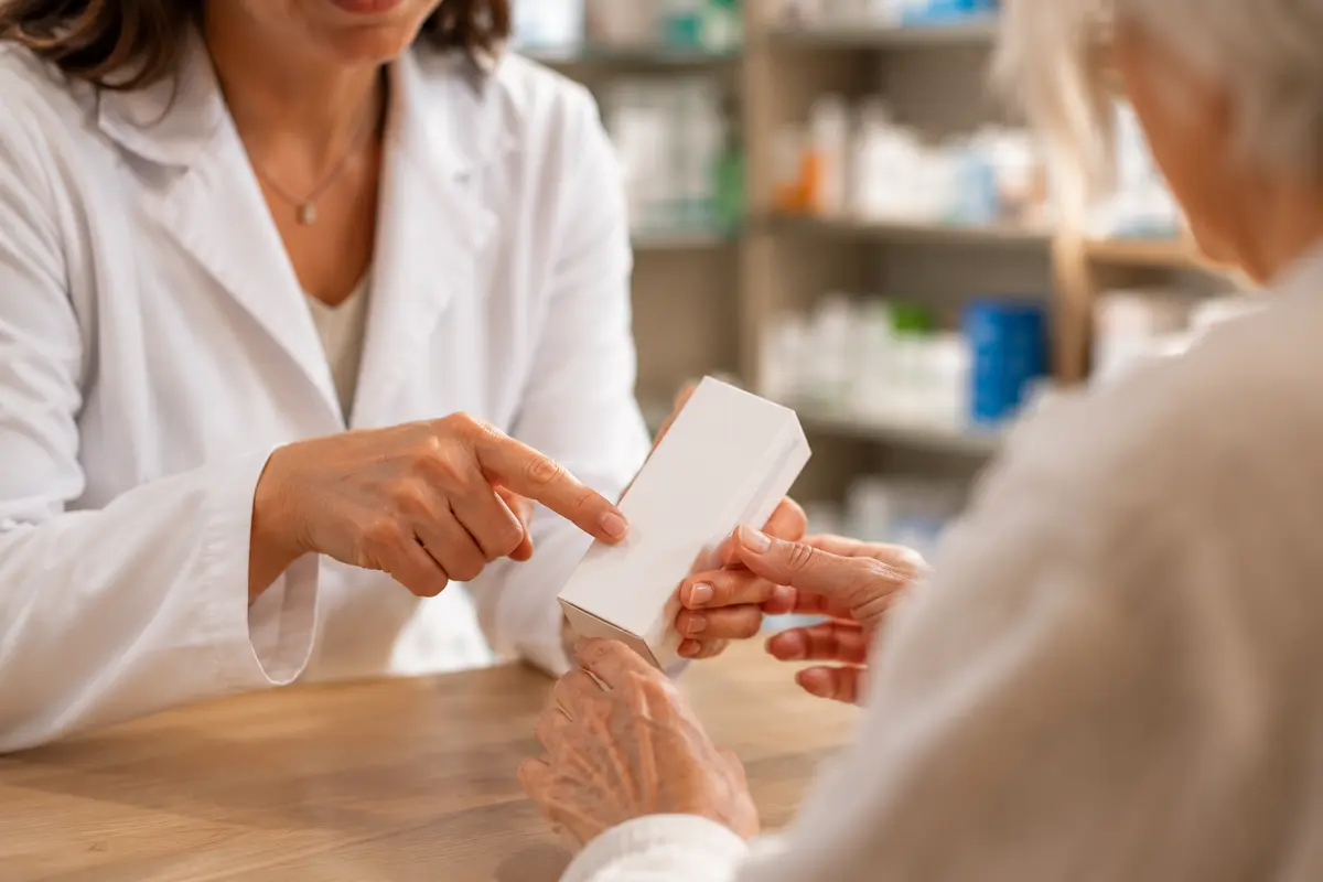 Farmacistă explicând unui pacient cum se administrează un medicament la ghișeul farmaciei