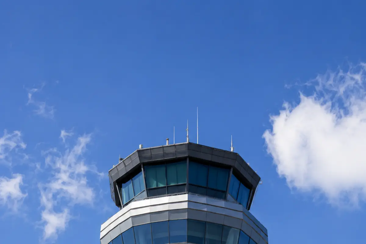 Turn de control al unui aeroport văzut de jos, cu structura de sticlă în vârf, pe cer senin